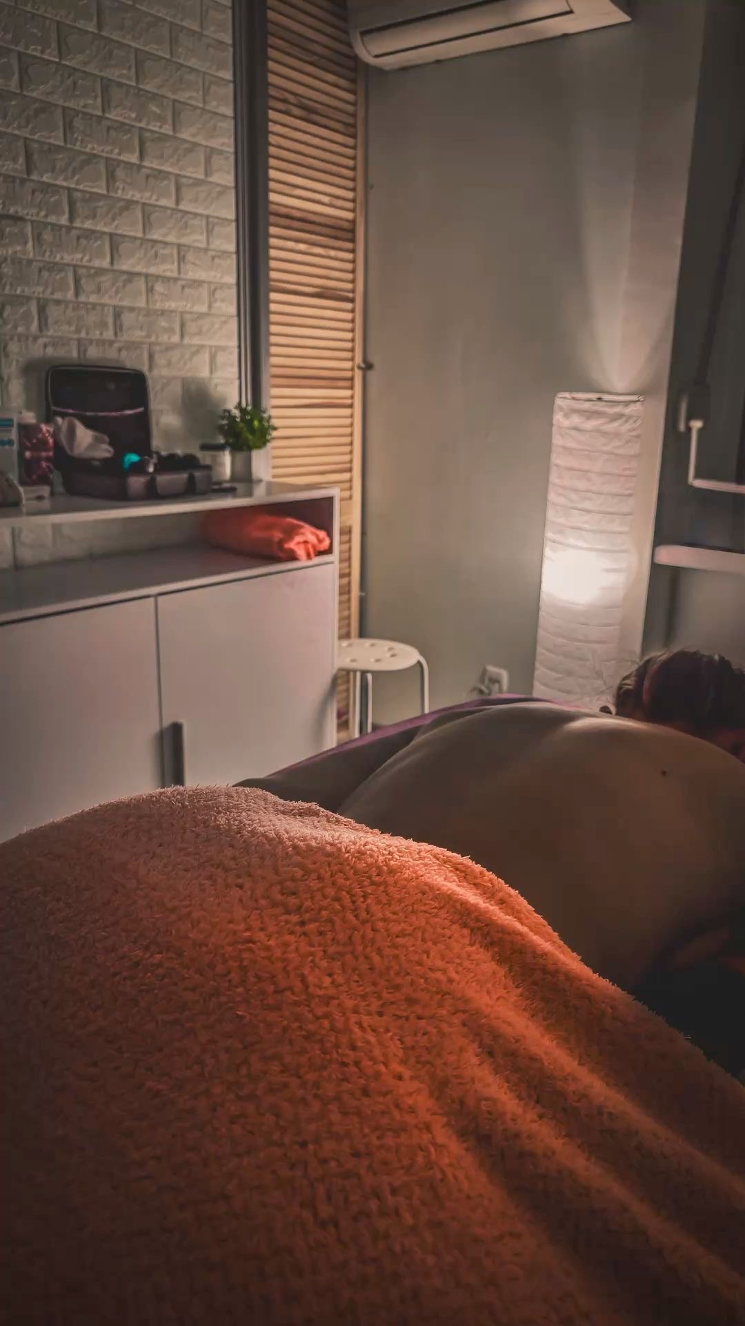 Client resting under a warm blanket during a massage in a softly lit room